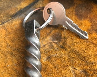 May include: A silver key attached to a twisted metal keychain. The keychain is made of a thick, twisted metal rod.
