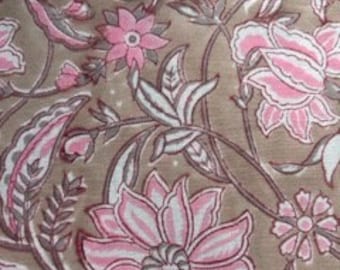 May include: Close-up of a fabric with a floral pattern. The design features large pink flowers with white and gray accents, set against a tan background. The leaves and stems are in shades of gray and pink.