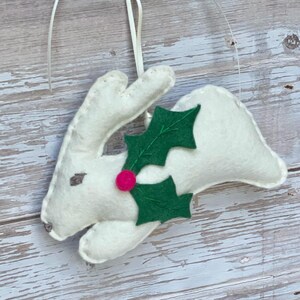 May include: White felt reindeer ornament with green felt holly leaves and a pink felt berry.