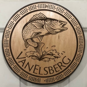 May include: A wooden circular game board with a fish jumping out of the water. The board has a numbered track around the edge and the words "VANELSBERG" and "Skunk" printed on it.