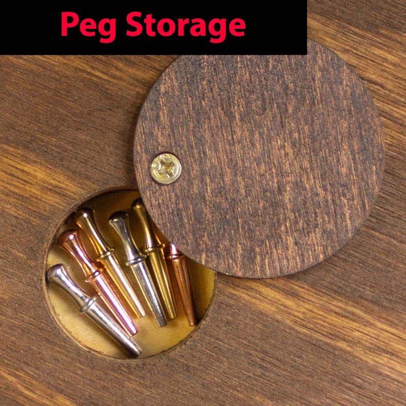 May include: A wooden box with a round lid that opens to reveal a compartment for storing small items. The compartment contains several small, colorful metal pegs.