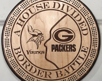 May include: A wooden game board with a circular shape. The board is divided into two sections, one for the Green Bay Packers and one for the Minnesota Vikings. The board has a brown border with the words "A House Divided Border Battle" printed on it. The board has a grid of holes around the edge, with numbers printed next to each hole.