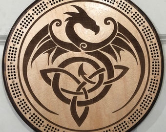 May include: A wooden cribbage board with a Celtic knot and dragon design. The board has a dark brown stain and a light wood background. The numbers 5 to 120 are printed around the edge of the board.