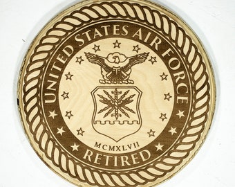 May include: A wooden round plaque with a brown engraved design of the United States Air Force seal. The seal includes an eagle with outstretched wings, a shield with stars and a sword, and the text "United States Air Force". Below the seal is the text "MCMXLVII RETIRED".