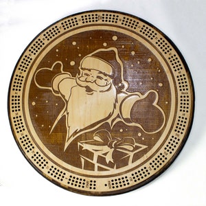 May include: A wooden cribbage board with a Santa Claus design. The board has a brown background with a white Santa Claus holding a gift. The board has a circular shape with a numbered track around the edge. The numbers on the track go from 1 to 120. The board also has a "Start" and "Finish" marker.