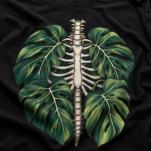May include: A black t-shirt featuring a central graphic print of a human rib cage and spine. The skeletal structure is flanked by four large, detailed green monstera leaves that appear to grow from behind the bones, creating a botanical design.