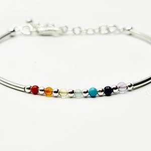 May include: A silver bracelet featuring a line of colourful gemstone beads. The beads are red, orange, yellow, green, blue and purple.