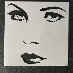 May include: Black and white stencil of a woman's face with large eyes, a small nose, and full lips. The stencil is made of a thin, flexible material and is designed for use with paint or other mediums.