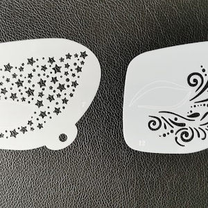 以下が含まれることがあります： ケーキやその他のクラフトを飾るための、白いプラスチック製のステンシル2枚。1枚は星形のデザイン、もう1枚は渦巻く花柄のデザインです。