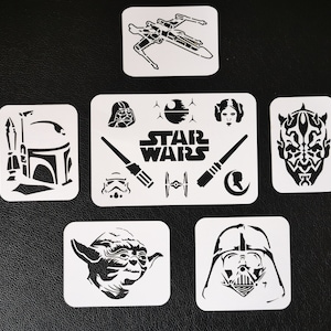 May include: Set of 10 white plastic stencils featuring Star Wars characters and symbols. The stencils include Darth Vader, Yoda, Boba Fett, Princess Leia, a TIE fighter, and the Death Star.