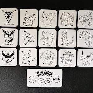 以下が含まれることがあります： 様々なポケモンのキャラクターとチームロゴの黒い線画が描かれた白い正方形のコースターのコレクション。コースターには、ピカチュウ、フシギダネ、ヒトカゲなどが含まれており、「Pokémon GO」のロゴも含まれています。