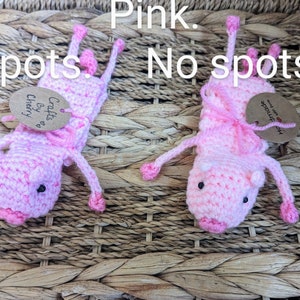 May include: Two pink crocheted pig finger puppets. One has pink and white spots, the other is solid pink. Both have black eyes and pink snouts. The pig with spots has a tag that says "Crafts by Cherry". The solid pink pig has a tag that says "Handmade with love".