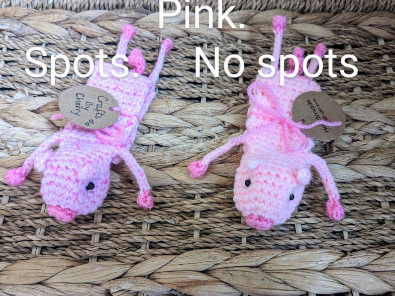 May include: Two pink crocheted pig finger puppets. One has pink and white spots, the other is solid pink. Both have black eyes and pink snouts. The pig with spots has a tag that says "Crafts by Cherry". The solid pink pig has a tag that says "Handmade with love".