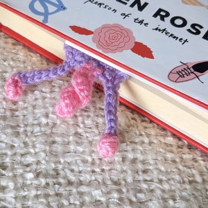 May include: A purple and pink crocheted bookmark with a curled tail, sticking out from the edge of a book titled "Modern Rose: The Person of the Internet".