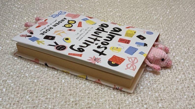 May include: A white book with a pink pig bookmark sticking out of it. The book cover has a colorful design with the title "Almost Everything" and the author's name "ARDEN ROSE".