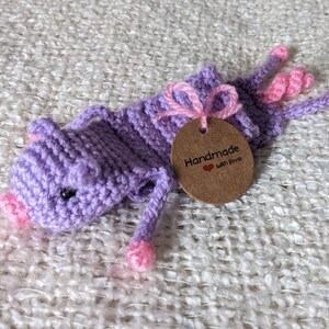 May include: Purple crocheted pig bookmark with pink accents and a brown tag that reads "Handmade with Love".