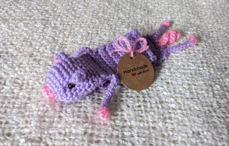 May include: Purple crocheted pig bookmark with pink accents and a brown tag that reads "Handmade with Love".