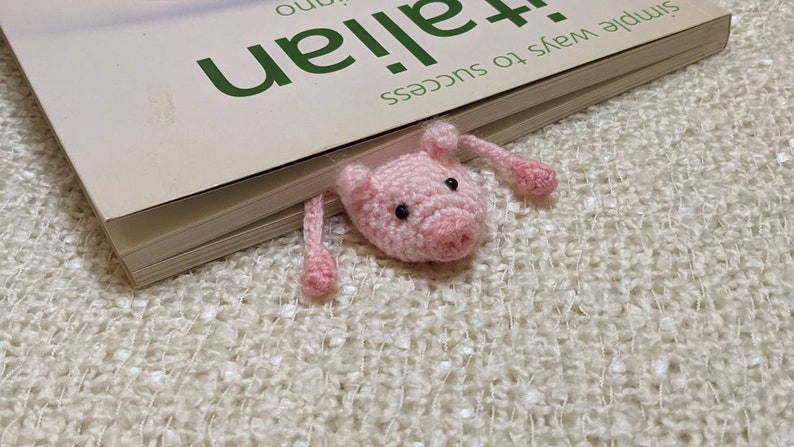 A pink crocheted pig bookmark peeking out from the edge of a book.