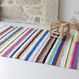 Puede incluir: Una alfombra de rayas coloridas con flecos en los bordes. La alfombra est&aacute; hecha de un material suave y texturizado y tiene una variedad de colores, incluyendo rojo, naranja, amarillo, verde, azul, morado y marr&oacute;n.