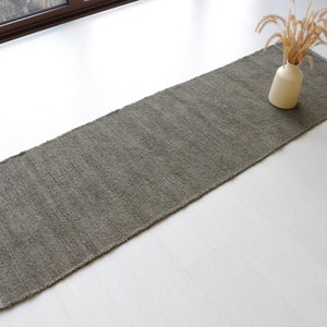 May include: A long, rectangular, gray rug with a textured surface. The rug is on a white floor.