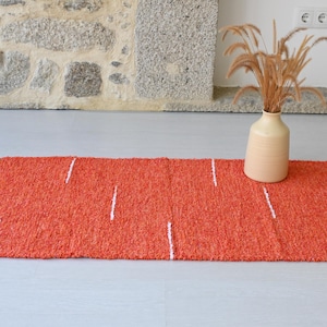 May include: A bright orange rug with white stripes. The rug is made of a soft, textured material and has a simple, modern design.