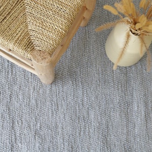 May include: A light gray woven rug with a woven chair and a vase of dried grass in the upper right corner.