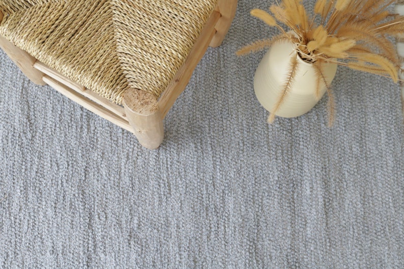 May include: A light gray woven rug with a woven chair and a vase of dried grass in the upper right corner.