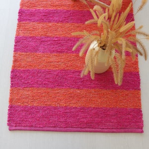 May include: A pink and orange striped woven rug with a vase of dried flowers on top.