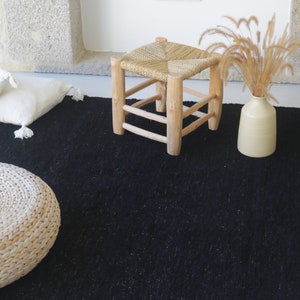 May include: A black woven rug with a white woven stool, a white woven pouf, and a white vase with dried grass.