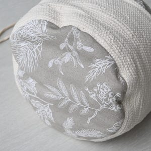 Pu&ograve; includere: Una borsa rotonda in tessuto bianco sporco con chiusura a coulisse. L'interno &egrave; grigio con una stampa botanica bianca di foglie e bacche. L'esterno &egrave; un materiale tessuto e strutturato.
