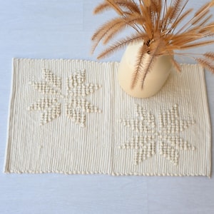 May include: A cream-colored woven rug with a raised floral design. The rug is made of natural fibers and has a fringed edge.