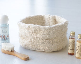 Può includere: Un cesto intrecciato bianco con una spazzola bianca, una bottiglia di bagnoschiuma per bambini etichettata "Bebés & Mamá" e due bottiglie di liquido marrone.