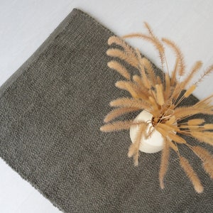 May include: A dark gray rug with a textured surface. A vase with dried beige grass is placed on the rug.