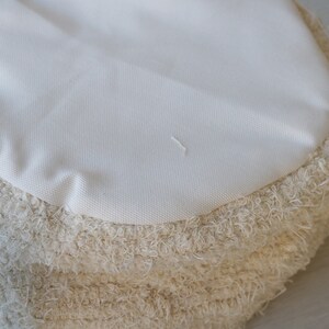 May include: A round, cream-colored pouf with a fluffy, shaggy texture. The pouf has a smooth, white fabric top.
