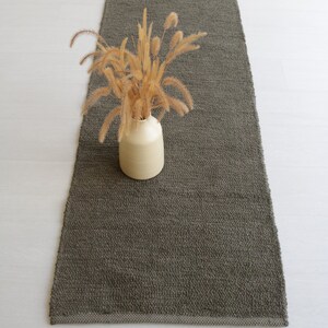 May include: A long, rectangular, dark green rug with a textured surface. A vase with dried flowers sits on the rug.