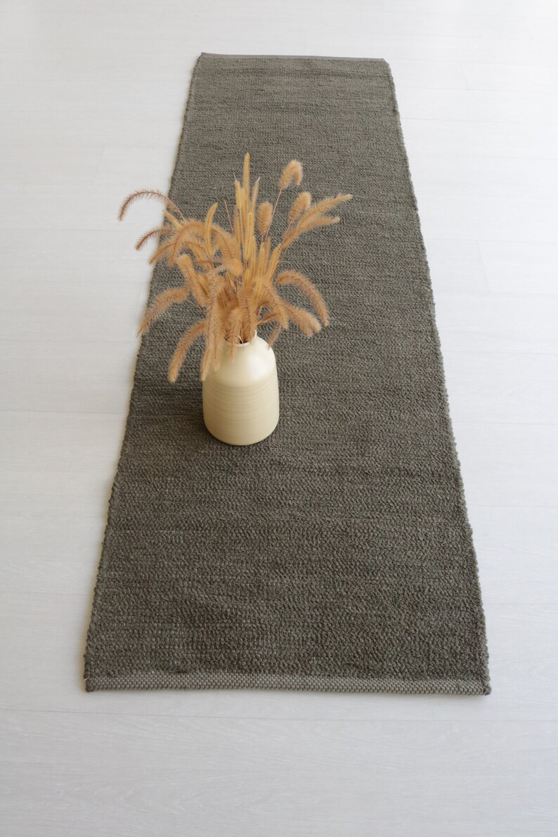 May include: A long, rectangular, dark green rug with a textured surface. A vase with dried flowers sits on the rug.