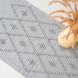 Puede incluir: Una alfombra gris y blanca con un patr&oacute;n texturizado. La alfombra tiene un patr&oacute;n de diamante con peque&ntilde;os c&iacute;rculos en relieve.