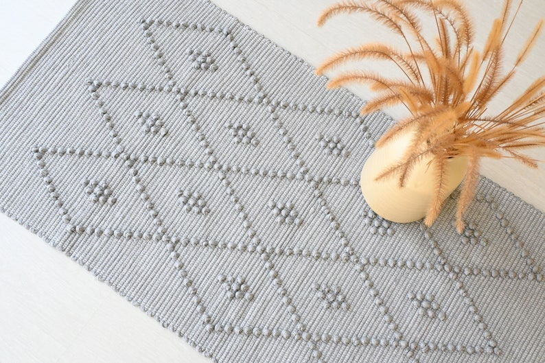 Puede incluir: Una alfombra gris y blanca con un patr&oacute;n texturizado. La alfombra tiene un patr&oacute;n de diamante con peque&ntilde;os c&iacute;rculos en relieve.