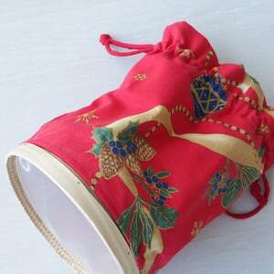 Pode incluir: Uma bolsa de tecido vermelho com cord&atilde;o de ajuste e um padr&atilde;o floral branco e dourado. A bolsa &eacute; forrada com uma malha branca e tem uma borda de madeira.