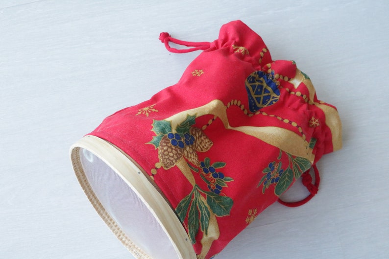 Pode incluir: Uma bolsa de tecido vermelho com cord&atilde;o de ajuste e um padr&atilde;o floral branco e dourado. A bolsa &eacute; forrada com uma malha branca e tem uma borda de madeira.