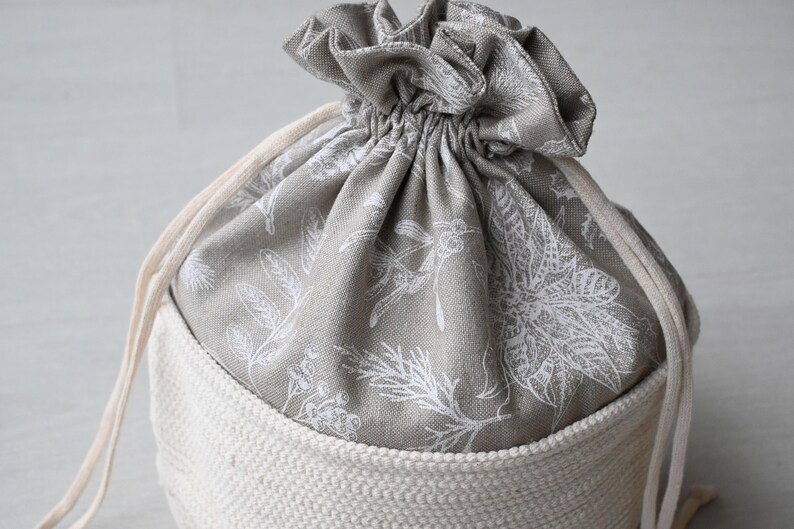 Pu&ograve; includere: Una borsa con coulisse con base in tessuto color crema e parte superiore a fantasia floreale grigia. La parte superiore &egrave; chiusa con una coulisse color crema. Il motivo floreale presenta disegni botanici bianchi.