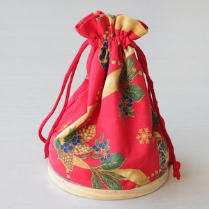 Pode incluir: Uma bolsa de cord&atilde;o vermelha com um padr&atilde;o floral dourado e verde. A bolsa est&aacute; sentada em uma base de madeira.