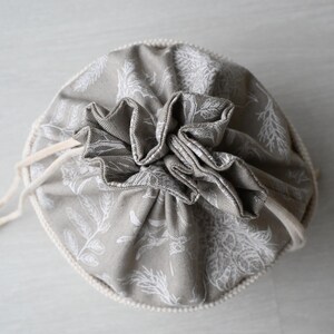 Pu&ograve; includere: Un sacchetto rotondo in tessuto grigio con chiusura a coulisse. Il sacchetto &egrave; decorato con un motivo botanico bianco e una parte superiore arricciata. Il cordino &egrave; di colore beige naturale.