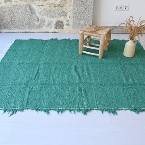 May include: A teal green woven rug with a fringed edge. A small wooden stool sits on the rug.
