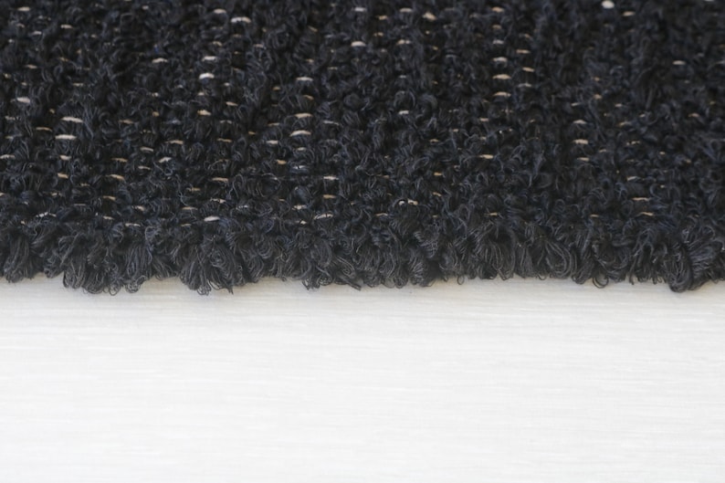 May include: Close-up of a black, textured fabric with a fringe edge. The fabric has a woven pattern with a subtle sheen.