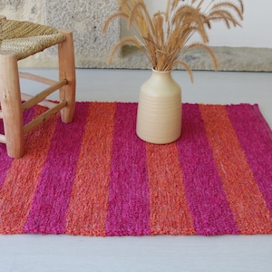 May include: A pink and orange striped rug with a wooden stool and a vase with dried flowers.