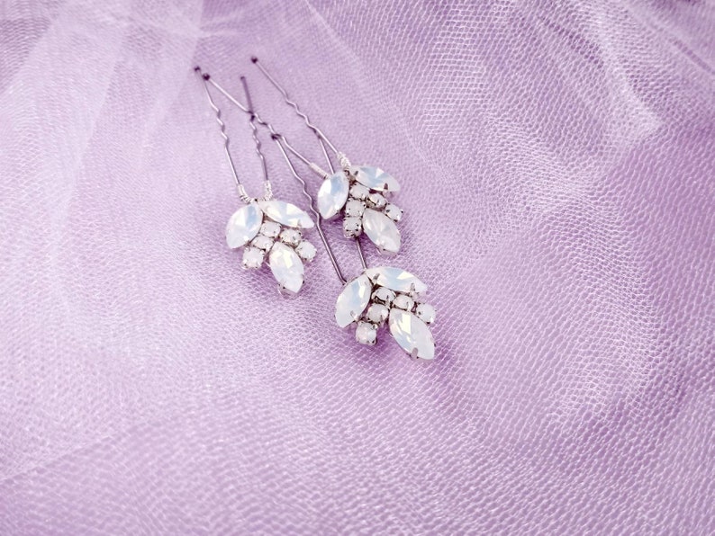 May include: Set of four silver hair pins with white opal-like stones arranged in a leaf design.