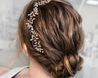 May include: A gold hair comb with crystal embellishments in a leaf design. The comb is worn in a woman's brown hair, styled in a low bun.