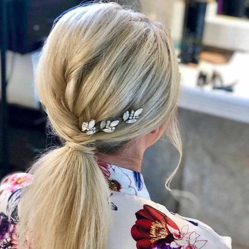 May include: A blonde woman with a low ponytail has four silver hair clips with clear rhinestones in her hair.