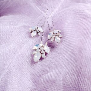 May include: Three silver hair pins with clusters of clear iridescent rhinestones. The pins are on a light purple fabric background.